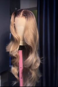 Perruque Lace HD blonde champagne avec longues ondulations glamour et racines foncées.
